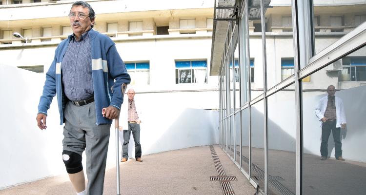 Hombre camina con su prótesis inferior apoyada en un bastón.