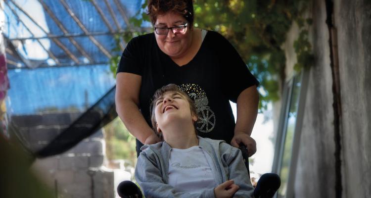 Acompañante lleva un niño sonriente en su silla de ruedas