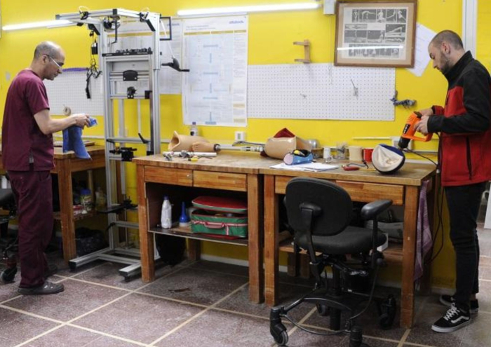 Dos personas trabajando en un taller de ortopedia. Sobre mesas de madera se ven herramientas y parte
