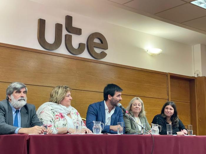 Autoridades de UTE y de MIDES en una mesa haciendo uso de la palabra. Detrás se ve el logo de UTE. Convenio entre UTE y MIDES