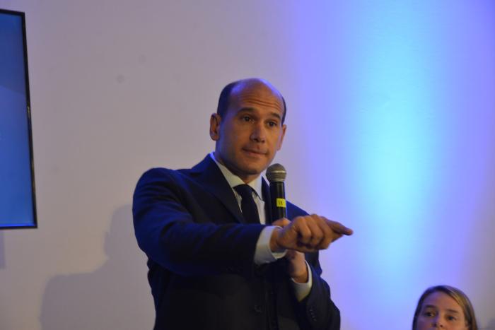 Ministro Lema durante su disertación Martín Lema con micrófono en mano, habla de pie habla a la audiencia . Sentada a su lado A. Brugman