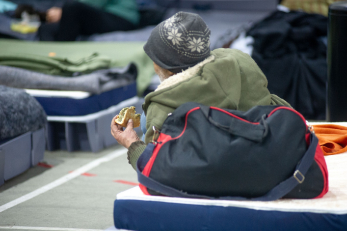 Persona sobre un colchón, de espaldas, comiendo una porción de alimento