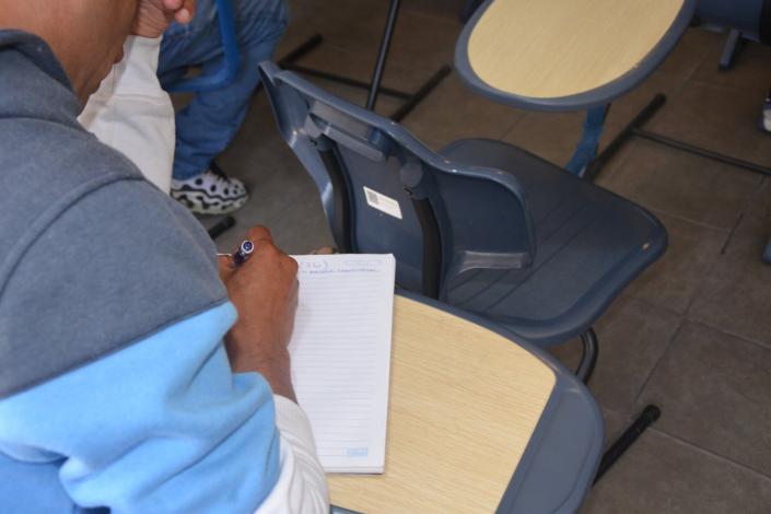 Estudiante en actitud pensativa escribe en cuaderno mientras se apoya en codo derecho
