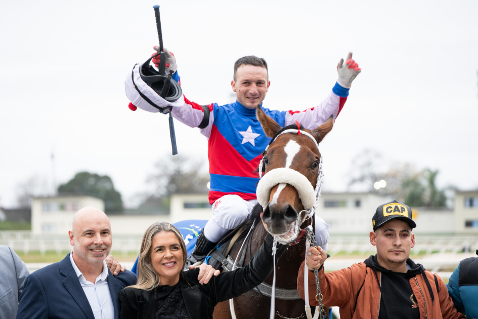 Jockey con los brazos alzados arriba de caballo ganador