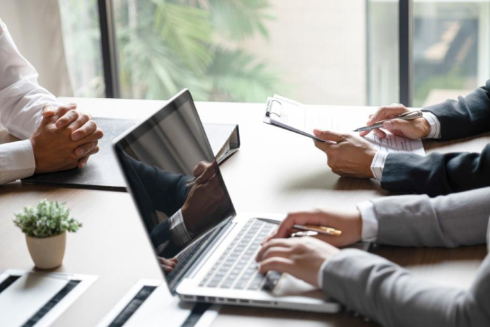 Persona trabajando en una computadora en reunión con dos personas