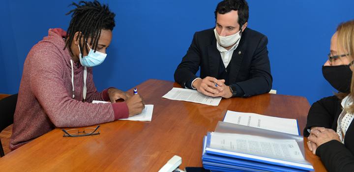 Persona beneficiaria de la beca, Director de Educación y encargada de la Oficina de becas firmando