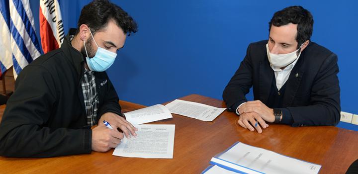 Persona beneficiaria de la beca y Director de Educación firmando contrato