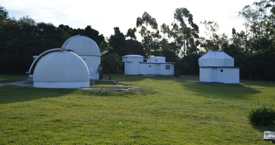 Observatorios astronómicos blancos en un predio de césped verde rodeado de árboles bajo un cielo claro.
