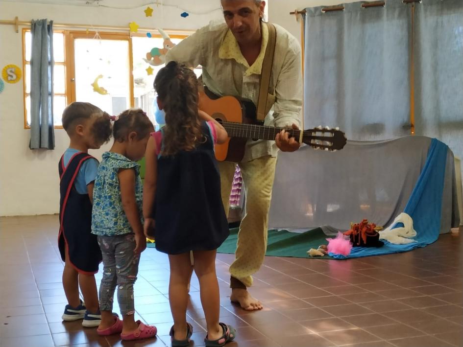 Músico con guitarra rodeado por grupo infantil