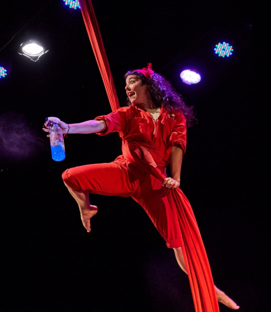Mujer colgada del techo rociando con perfumador a los espectadores