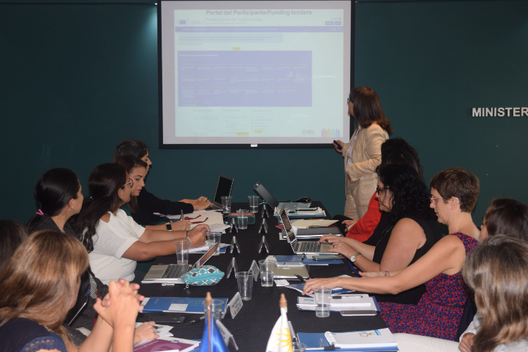 Claudia Romano exponiendo Personas sentadas al rededor de la mesa mirando la presentación proyectada