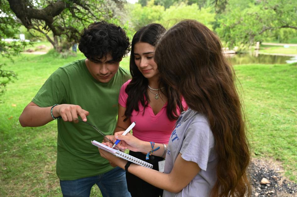 Tres jóvenes de pie mirando de cerca una libreta