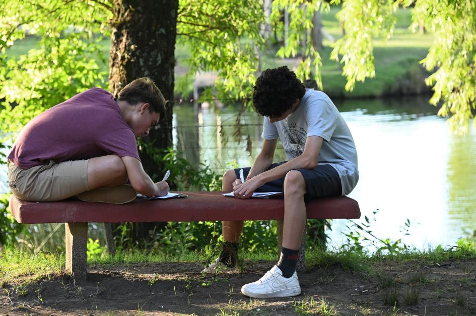 Dos jóvenes escribiendo sentados sobre un banco al aire libre