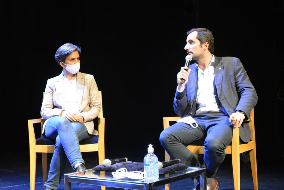 dos personas sentadas en escenario con micrófono hablando