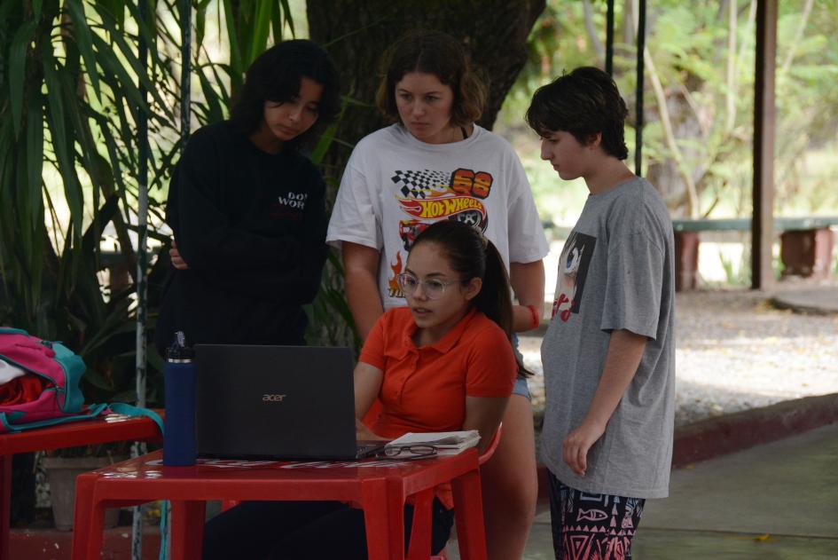 Tres personas de pie alrededor de una mujer sentada con una laptop
