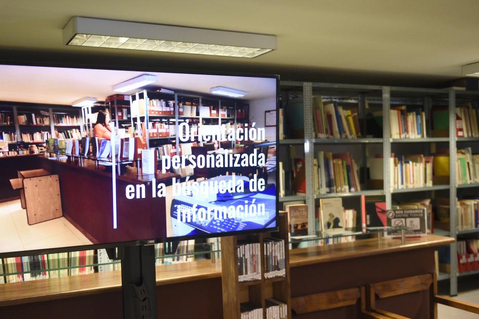 Estanterías con libros, pantalla con texto: Orientación personalizada en la búsqueda de información