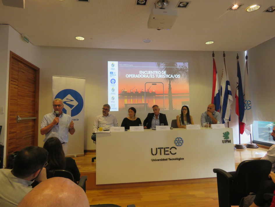 Encuentro de Rutas Unesco en Fray Bentos fortalece la promoción y gestión sostenible. Plano general de personas en mesa.