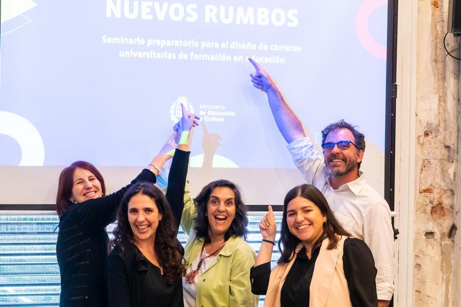 Docentes con el brazo levanto y señalando el cartel Nuevos Rumbos