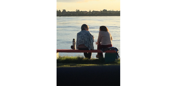 Dos personas conversando en un banco cerca del agua
