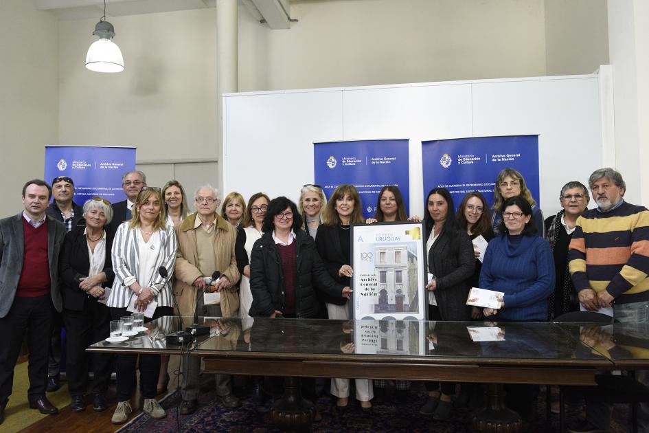 Foto de funcionarios junto al sello conmemorativo en la sala de actos del AGN. 