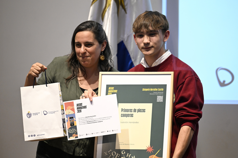 Alumno y docente sosteniendo la mención de categoría Narrativa Escrita 
