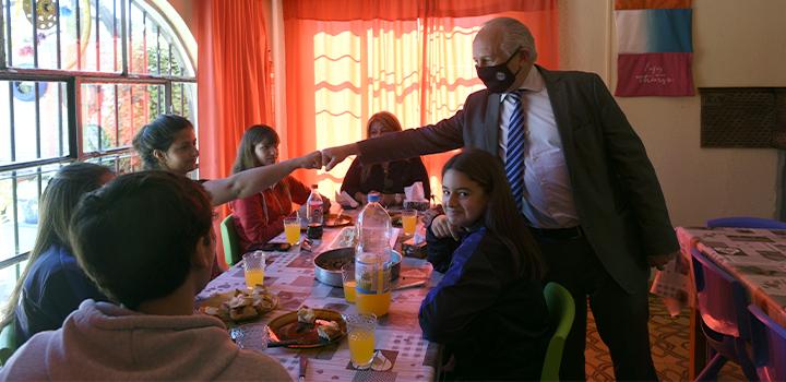 Ministro del MEC saludando con puño a personas que están sentadas en una mesa