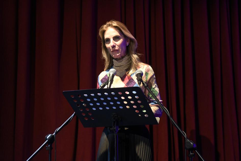 Mujer hablando frente a micrófono y atril.