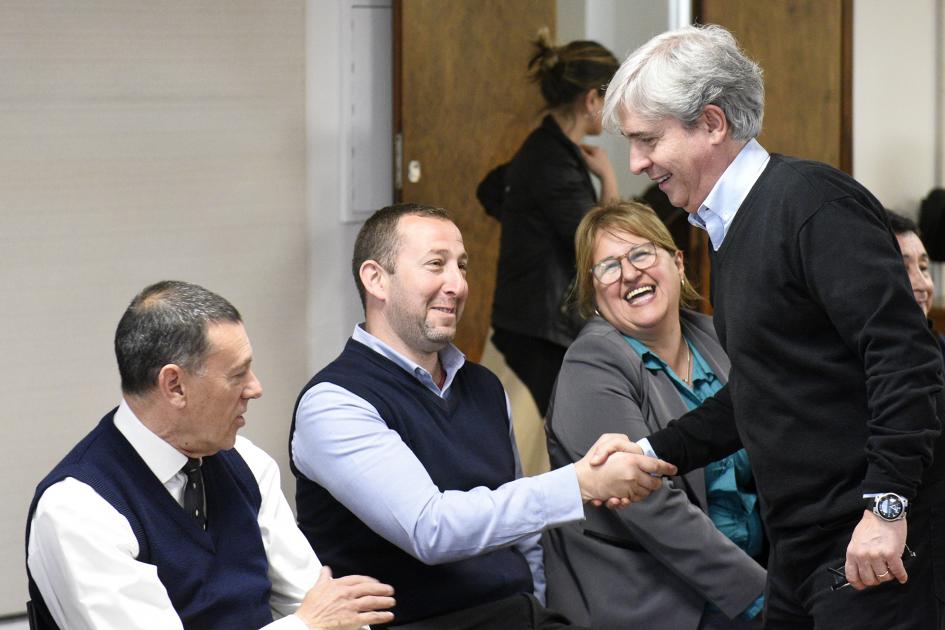 Persona parada saludando a otras personas sentadas.