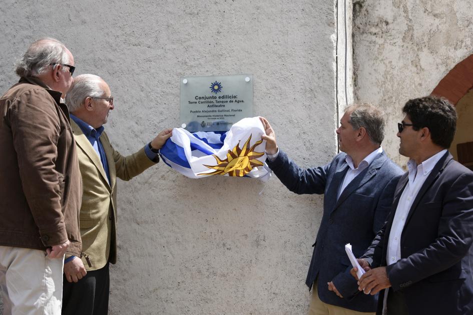 Personas quitando la bandera uruguaya de encima de una placa.