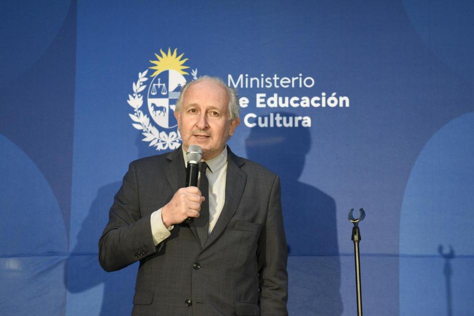 Ministro de Educación y Cultura hablando al público. De fondo está el logo del MEC.