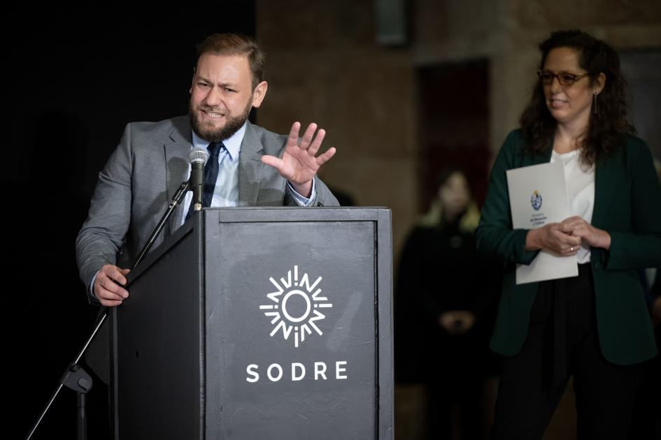 Hombre hablando atrás de un atril con la mano levantada