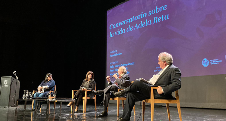 De izq. a der.: María Inés Obaldía, Ana Ribeiro, Julio María Sanguinetti y Juan Miguel Petit. Participantes del conversatorio sentados en sillas en el escenario de la sala.