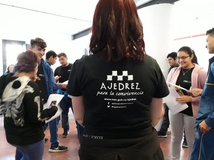 Ronda de jóvenes con referente del programa mujer de remera negra de espaldas con la inscripcion ajedrez para la convivencia