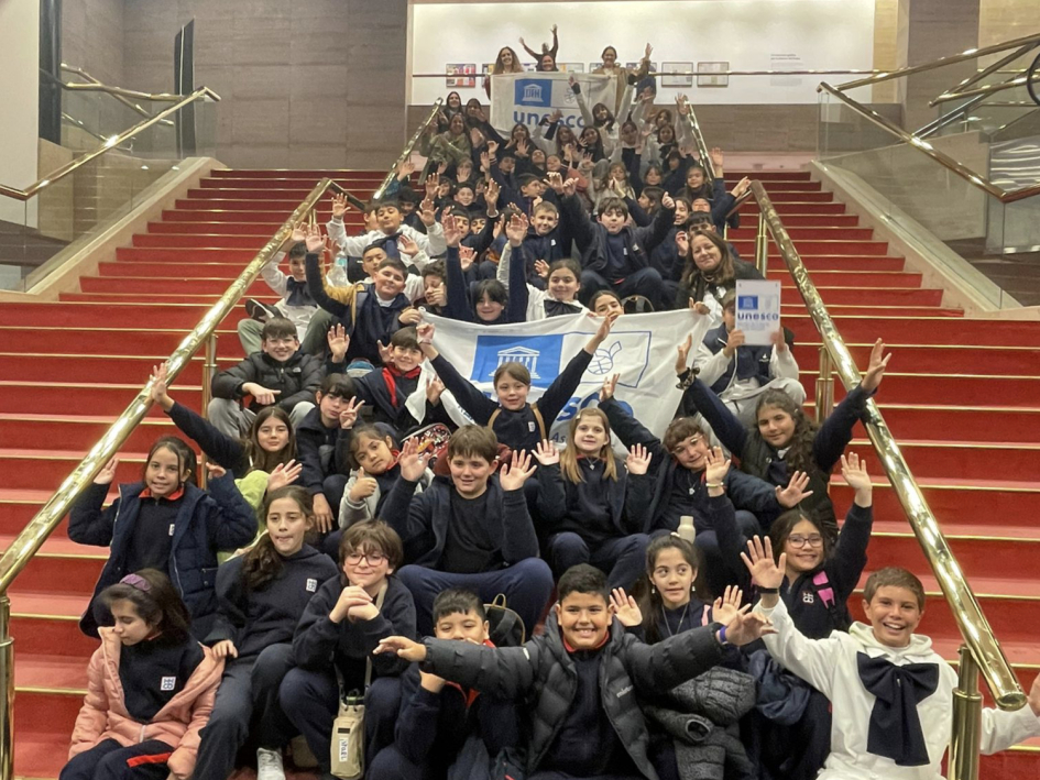 Arte, integración y cultura en la RedPEA Uruguay Niños, niñas y docentes sentados en la escalera del Auditorio Nacional Adela Reta saludando