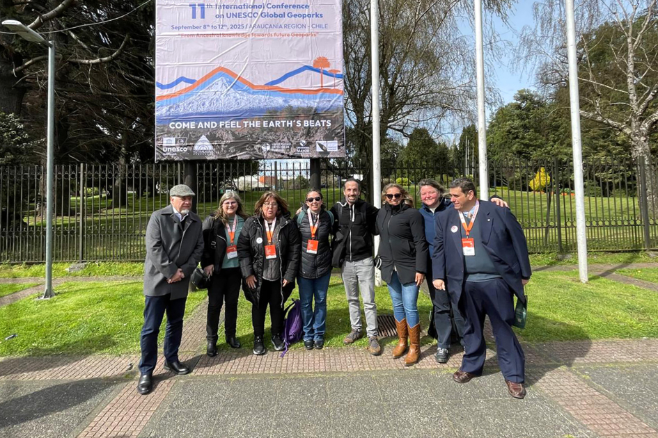 Grupo de personas frente a cartel del 11º Congreso Internacional de Geoparques UNESCO en Chile