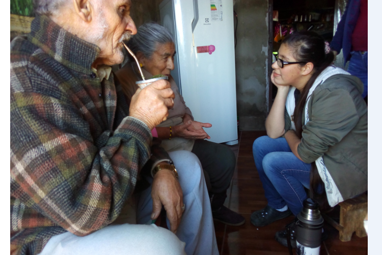 Niña mirando a dos personas mayores (sus abuelos) mientras toman mate