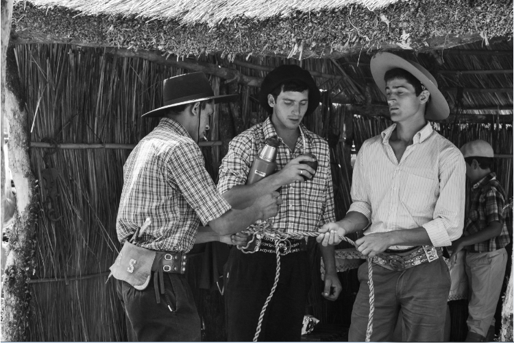 Tres gauchos tomando mate y trenzando