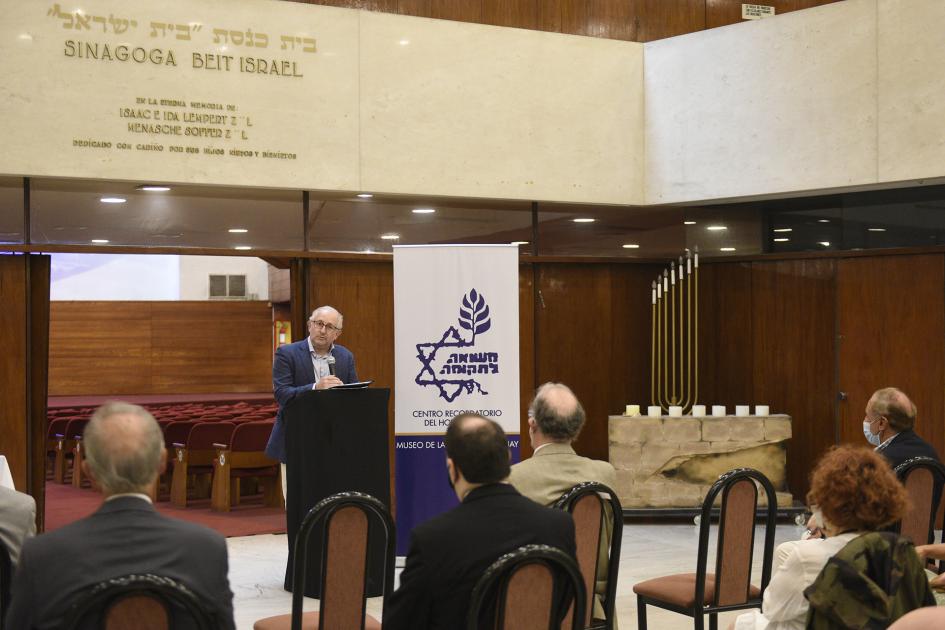 Ministro del MEC atrás de atril dando el discurso y a su lado, un banner. De espalda está la gente