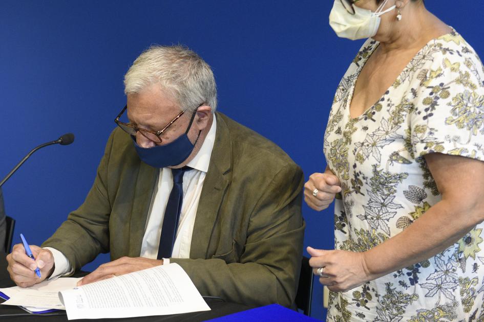 Hombre sentado, firmando la Carta Intención y a su lado hay una mujer mirando como firma