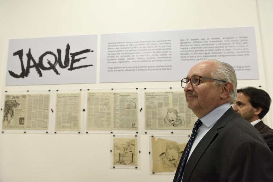 Hombre de lentes y de perfil y atrás se muestra la exposición y un cartel que dice Jaque