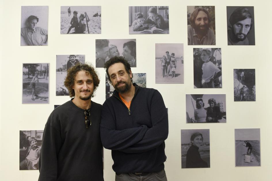 Dos hombres posando para la foto y atrás se ven fotos antiguas