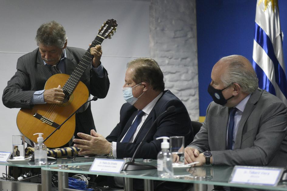 Payador tocando la guitarra y dos hombres sentados mirándolo