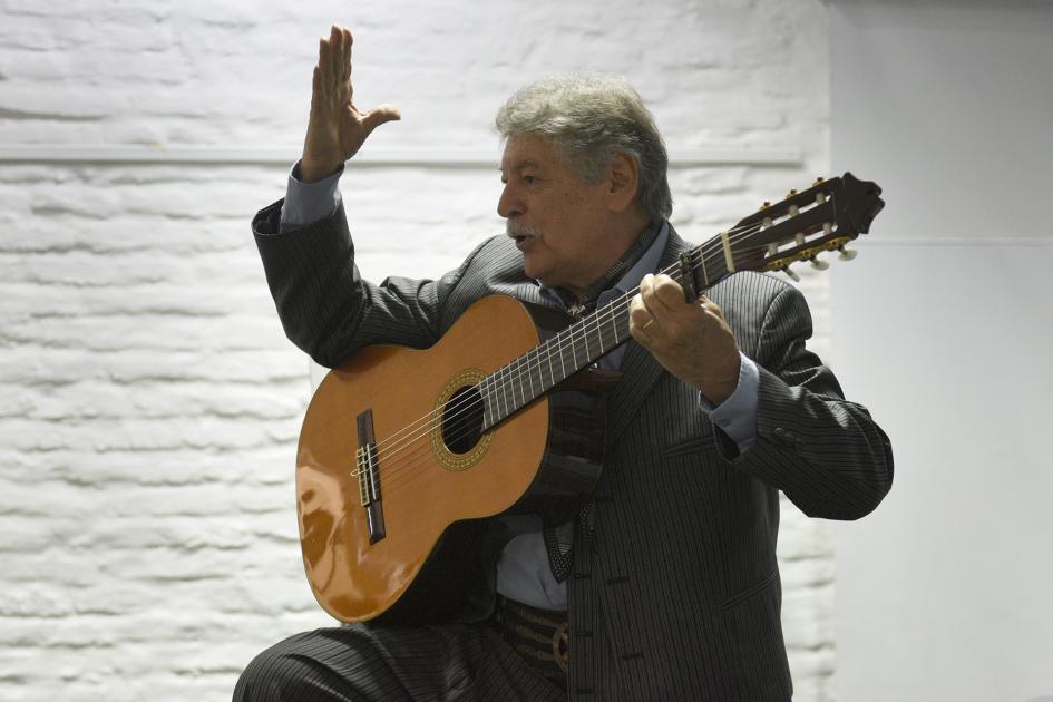 Hombre con la mano levantada y con guitarra apoyada en una pierna