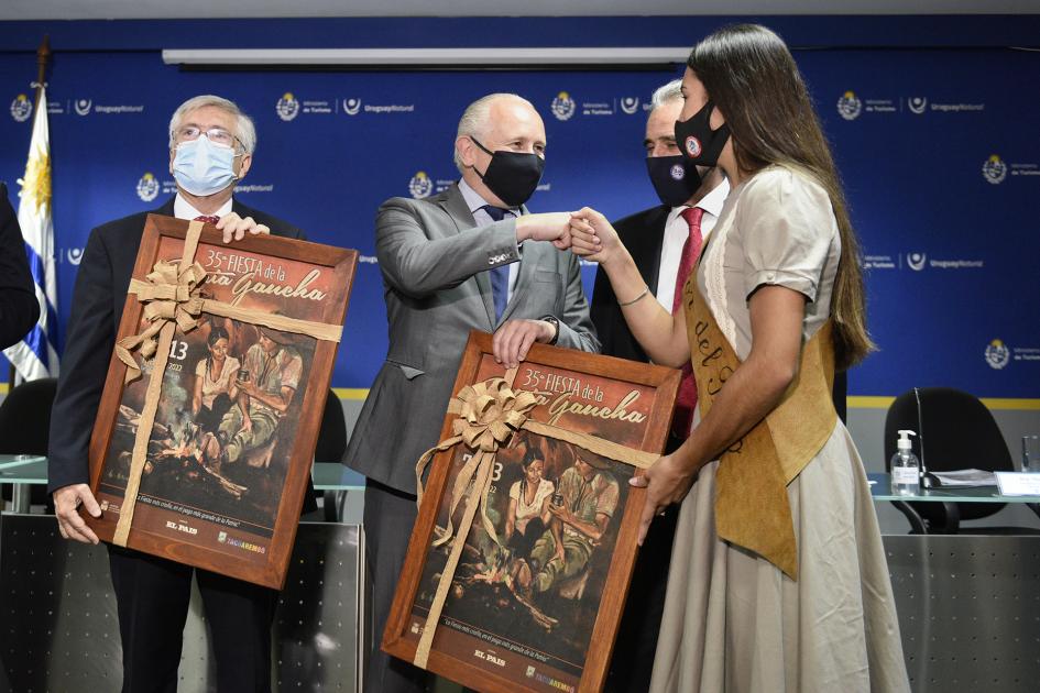 Dos hombres con un cuadro en la mano y el ministro saludando con un puño a la Flor del Pago