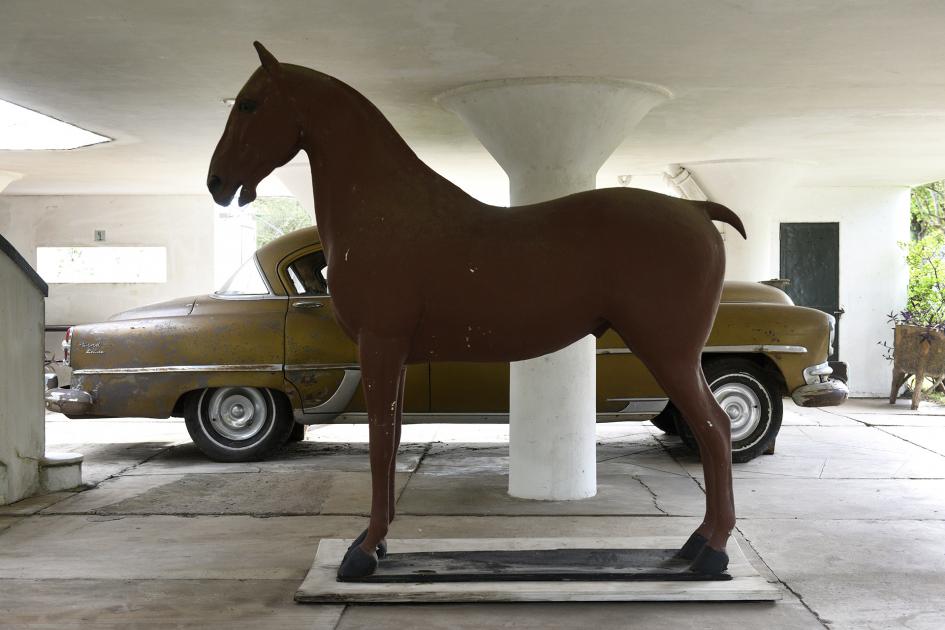 Escultura de un caballo y al fondo se ve un auto antiguo