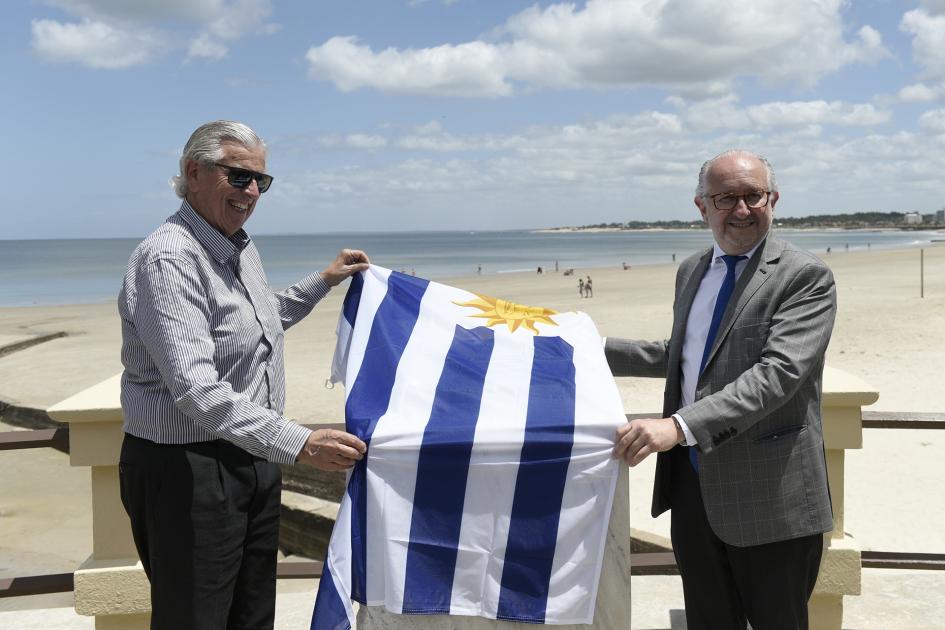 Dos hombres sonriendo y agarrando la bandera uruguaya para descubrir la placa