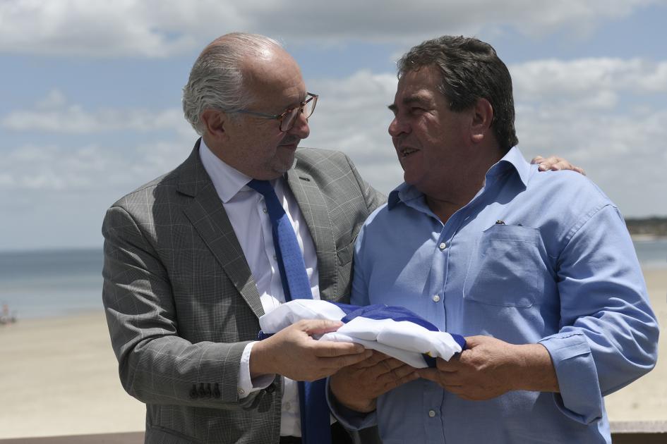 Dos hombres abrazados y mirándose. El ministro del MEC le entrega la bandera al alcalde