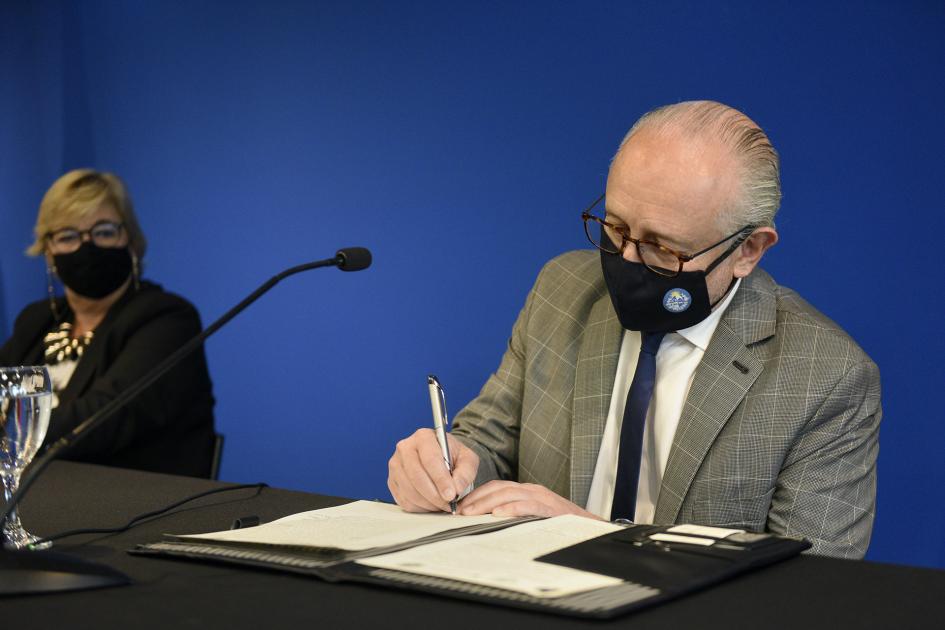 Hombre firmando un acta y a su izquierda una mujer lo está viendo