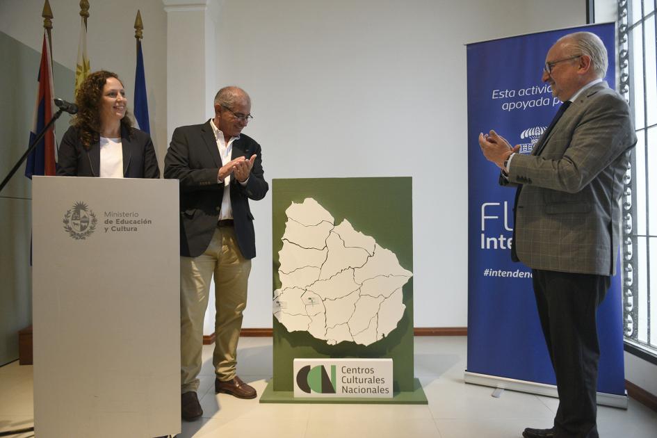 Dos hombre aplaudiendo y en el medio de ellos está el mapa de Uruguay