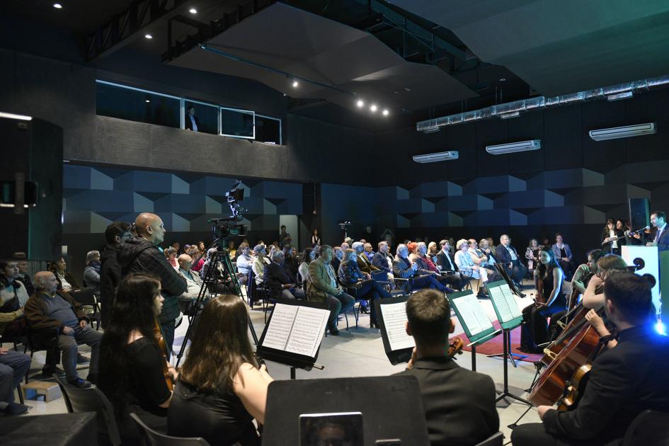 Vista general de la sala central con público sentado y de espalda los músicos del Sodre